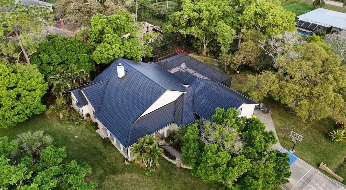 Aerial view of a large home with a navy metal roof surrounded by trees