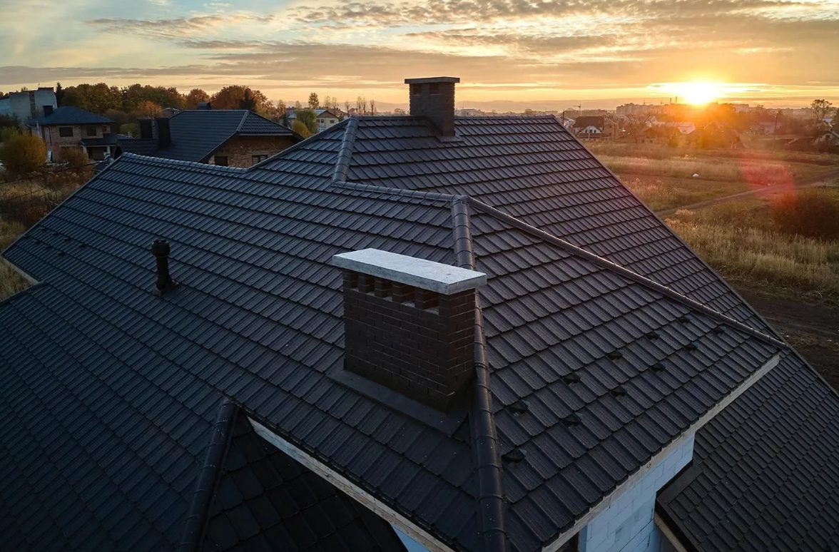 Dark standing-seam metal roof with chimney at sunset