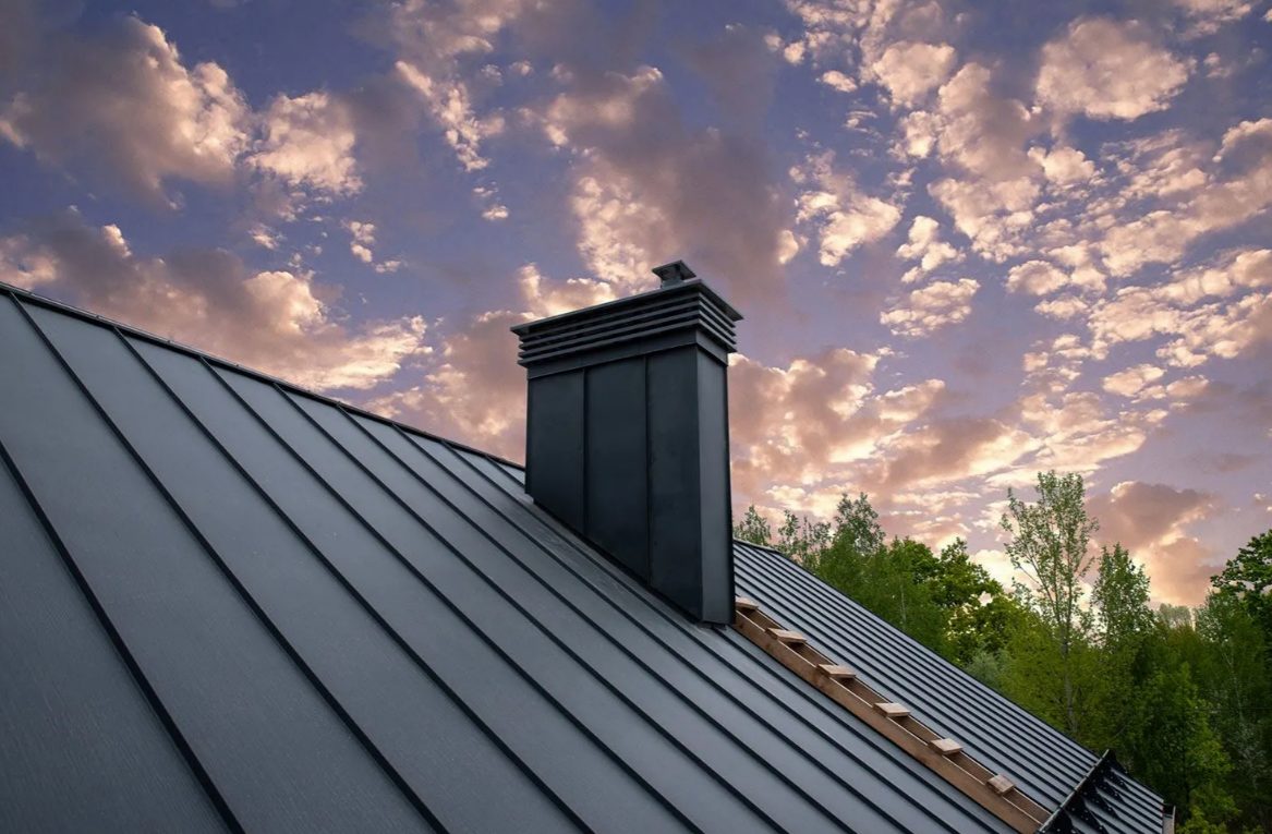 Standing-seam metal roof with a black chimney against a sunset sky